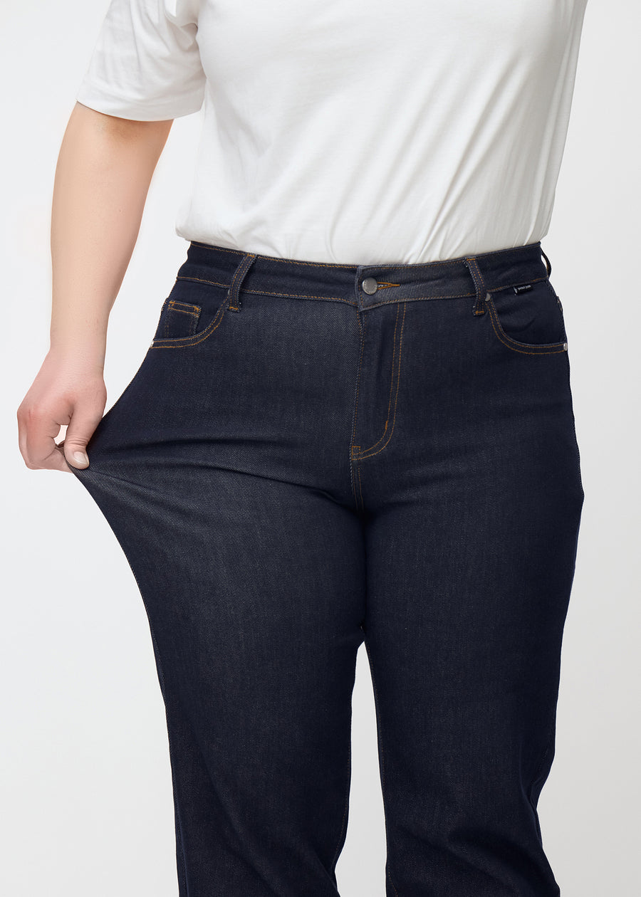 Plus size-modell sträcker den djupt mörkblå denimen jeans för kvinnor i färgen Midnights vid låret för att visa materialets stretch.