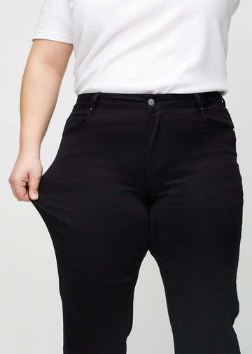 Regularjeans för kvinnor i svart, färgen Ravens. En plus size-modell drar i tyget vid låret för att visa stretchen.