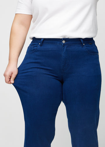 Regularjeans för kvinnor i mörkblå, färgen Royals. En plus size-modell drar i tyget vid låret för att visa stretchen.