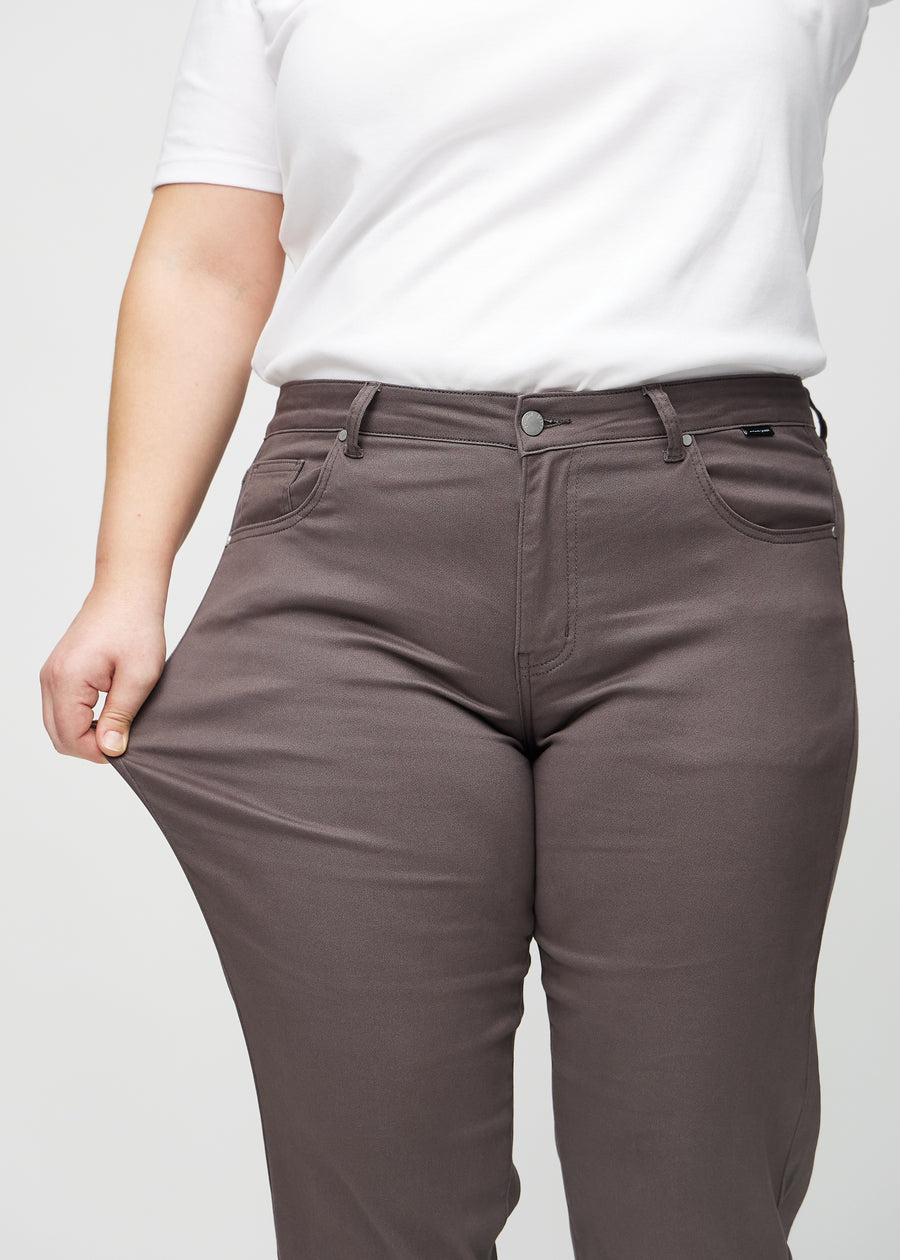 Regularjeans för kvinnor i gråbrun, färgen Thunders. En plus size-modell drar i tyget vid låret för att visa stretchen.