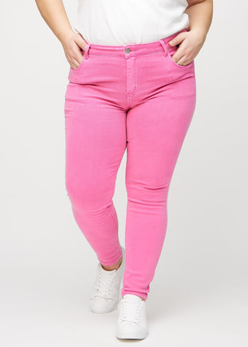 Skinnyjeans för kvinnor i ljusrosa, färgen Flamingos. Framifrån på en plus size-modell, med nära passform runt benen.