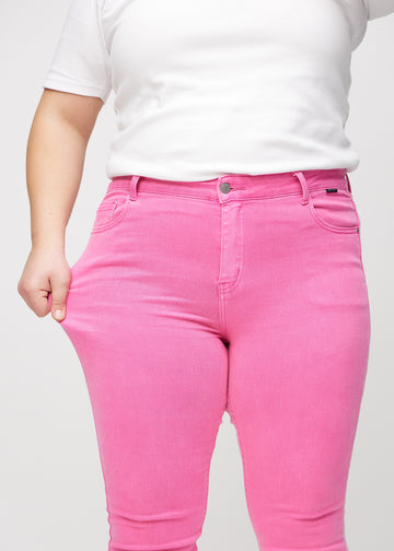 Skinnyjeans för kvinnor i ljusrosa, färgen Flamingos. En plus size-modell drar i jeanstyget vid låret för att visa stretchen.