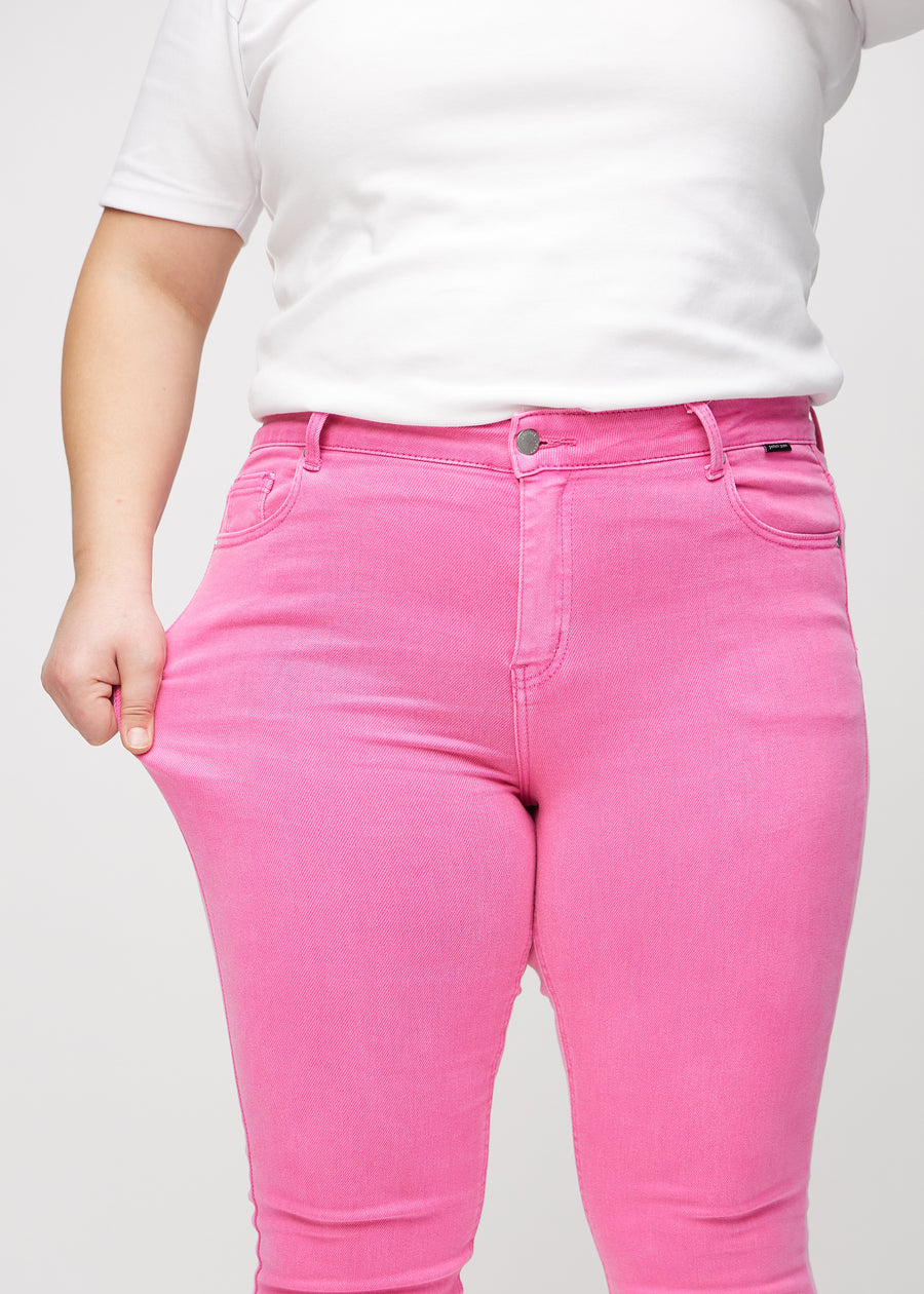 Skinnyjeans för kvinnor i ljusrosa, färgen Flamingos. En plus size-modell drar i jeanstyget vid låret för att visa stretchen.