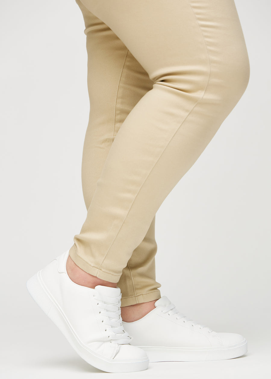 Skinnyjeans för kvinnor i beige, färgen Gazelles. Närbild vid anklarna på en plus size-modell som visar de åtsittande bensluten.