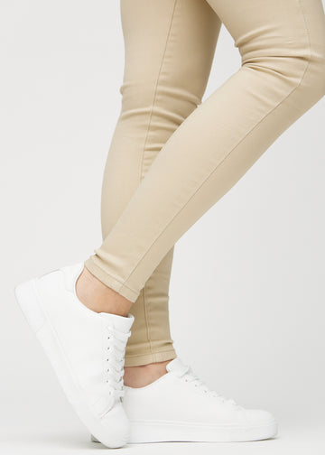 Skinnyjeans för kvinnor i beige, färgen Gazelles. Närbild vid anklarna på en modell som visar de åtsittande bensluten.