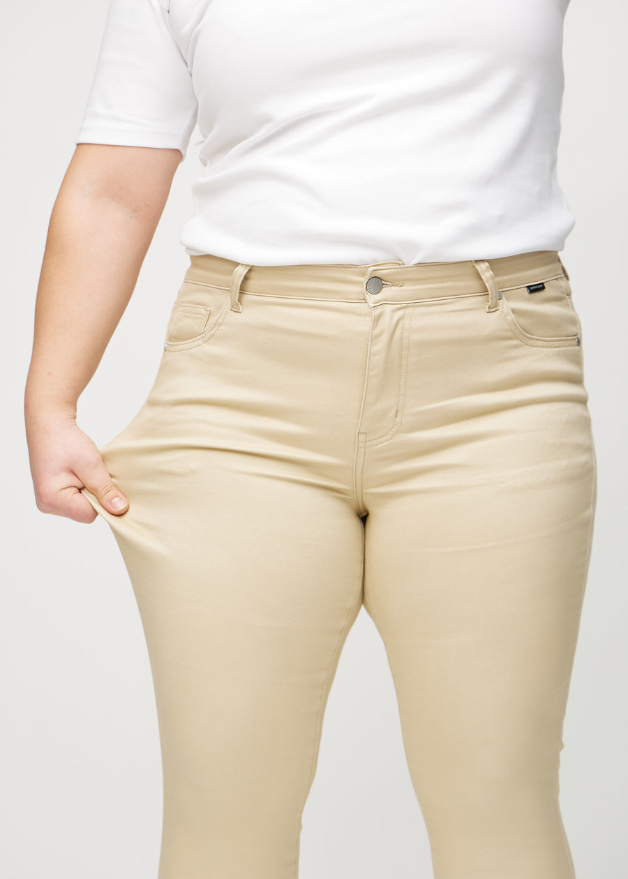 Skinnyjeans för kvinnor i beige, färgen Gazelles. En plus size-modell drar i jeanstyget vid låret för att visa stretchen.
