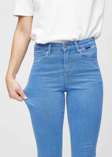 Skinnyjeans för kvinnor i blå, färgen Geraniums. En modell drar i jeanstyget vid låret för att visa stretchen.