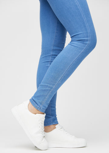 Skinnyjeans för kvinnor i blå, färgen Geraniums. Närbild vid anklarna på en modell som visar de åtsittande bensluten.