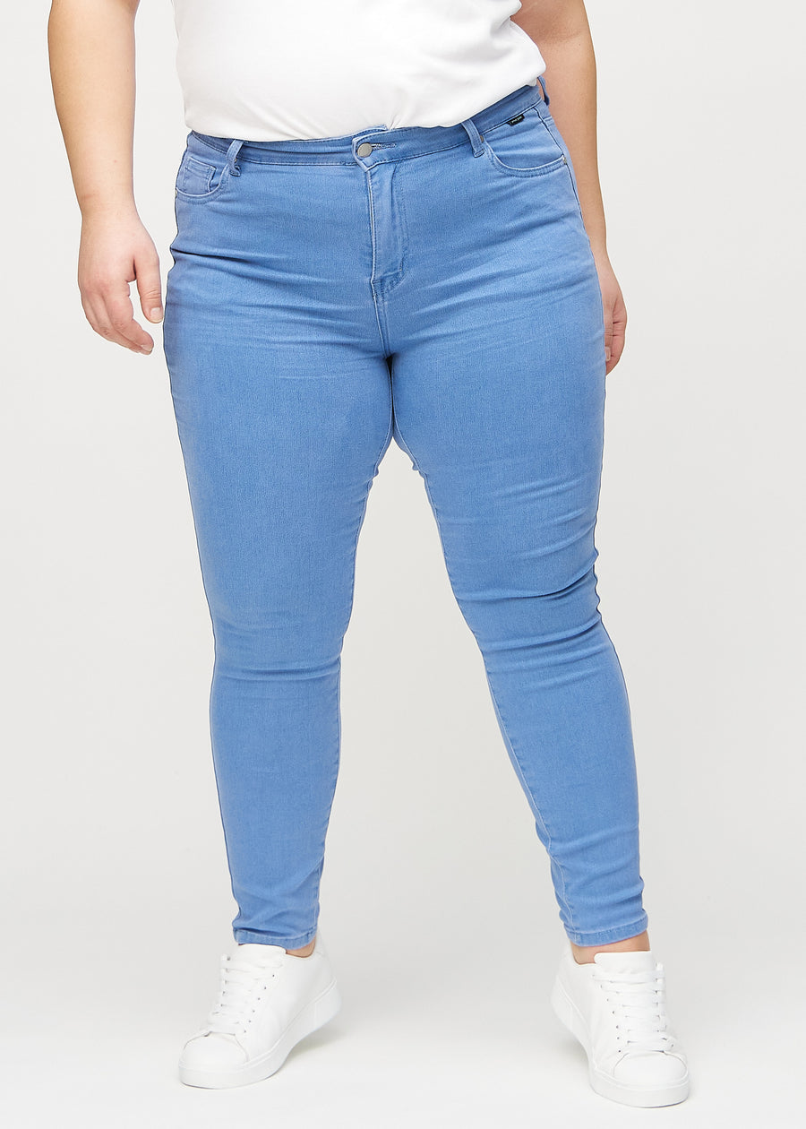 Skinnyjeans för kvinnor i blå, färgen Geraniums. Framifrån på en plus size-modell, med nära passform runt benen.