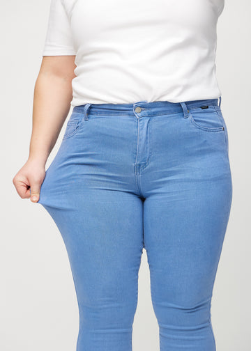 Skinnyjeans för kvinnor i blå, färgen Geraniums. En plus size-modell drar i jeanstyget vid låret för att visa stretchen.