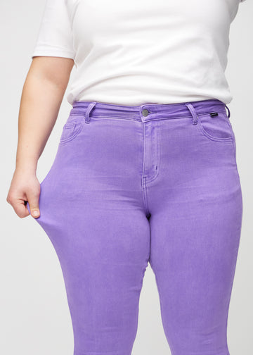 Skinnyjeans för kvinnor i lila, färgen Lavenders. En plus size-modell drar i jeanstyget vid låret för att visa stretchen.