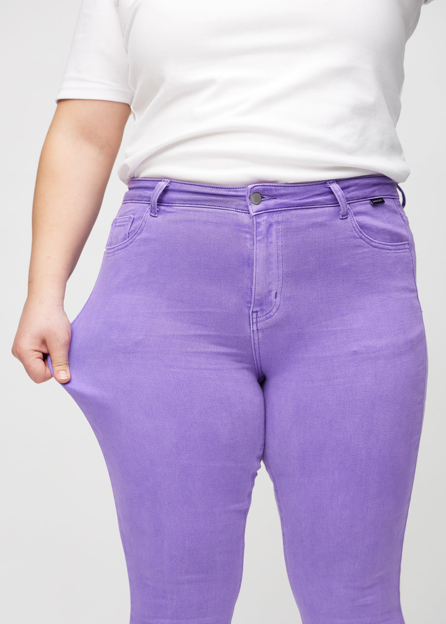 Skinnyjeans för kvinnor i lila, färgen Lavenders. En plus size-modell drar i jeanstyget vid låret för att visa stretchen.