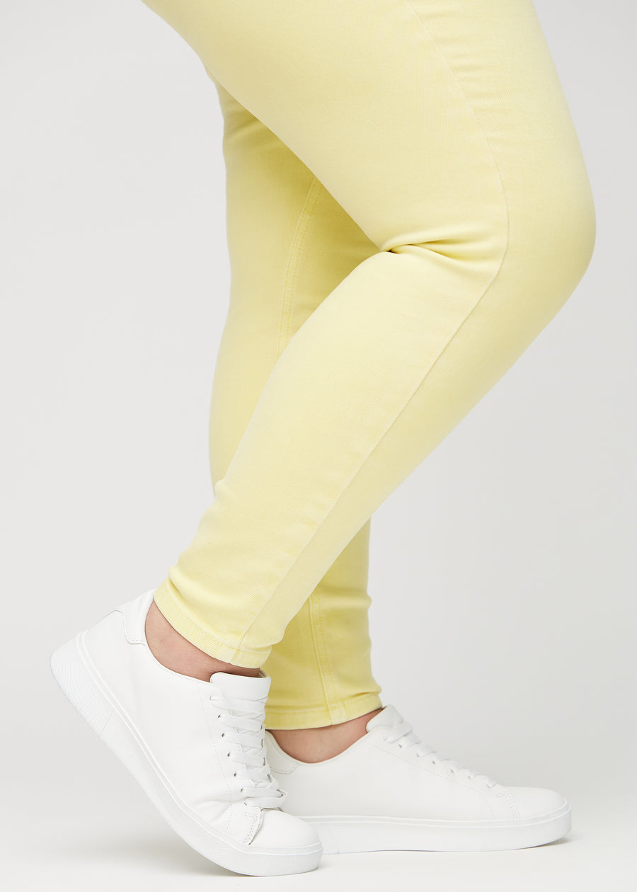 Skinnyjeans för kvinnor i ljusgul, färgen Lemonades. Närbild vid anklarna på en plus size-modell som visar de åtsittande bensluten.