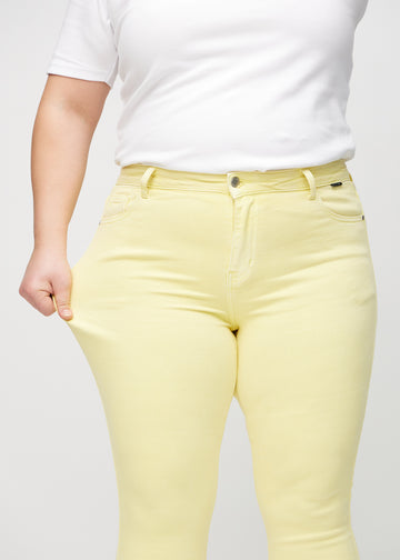 Skinnyjeans för kvinnor i ljusgul, färgen Lemonades. En plus size-modell drar i jeanstyget vid låret för att visa stretchen.