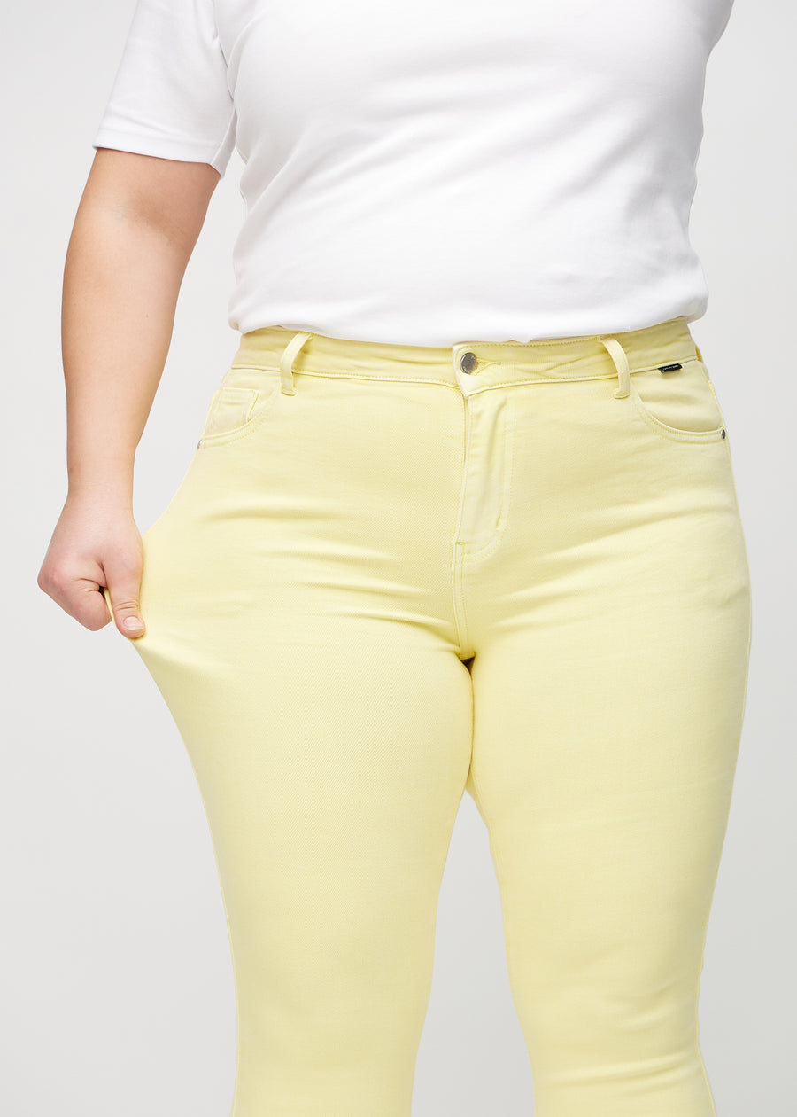 Skinnyjeans för kvinnor i ljusgul, färgen Lemonades. En plus size-modell drar i jeanstyget vid låret för att visa stretchen.