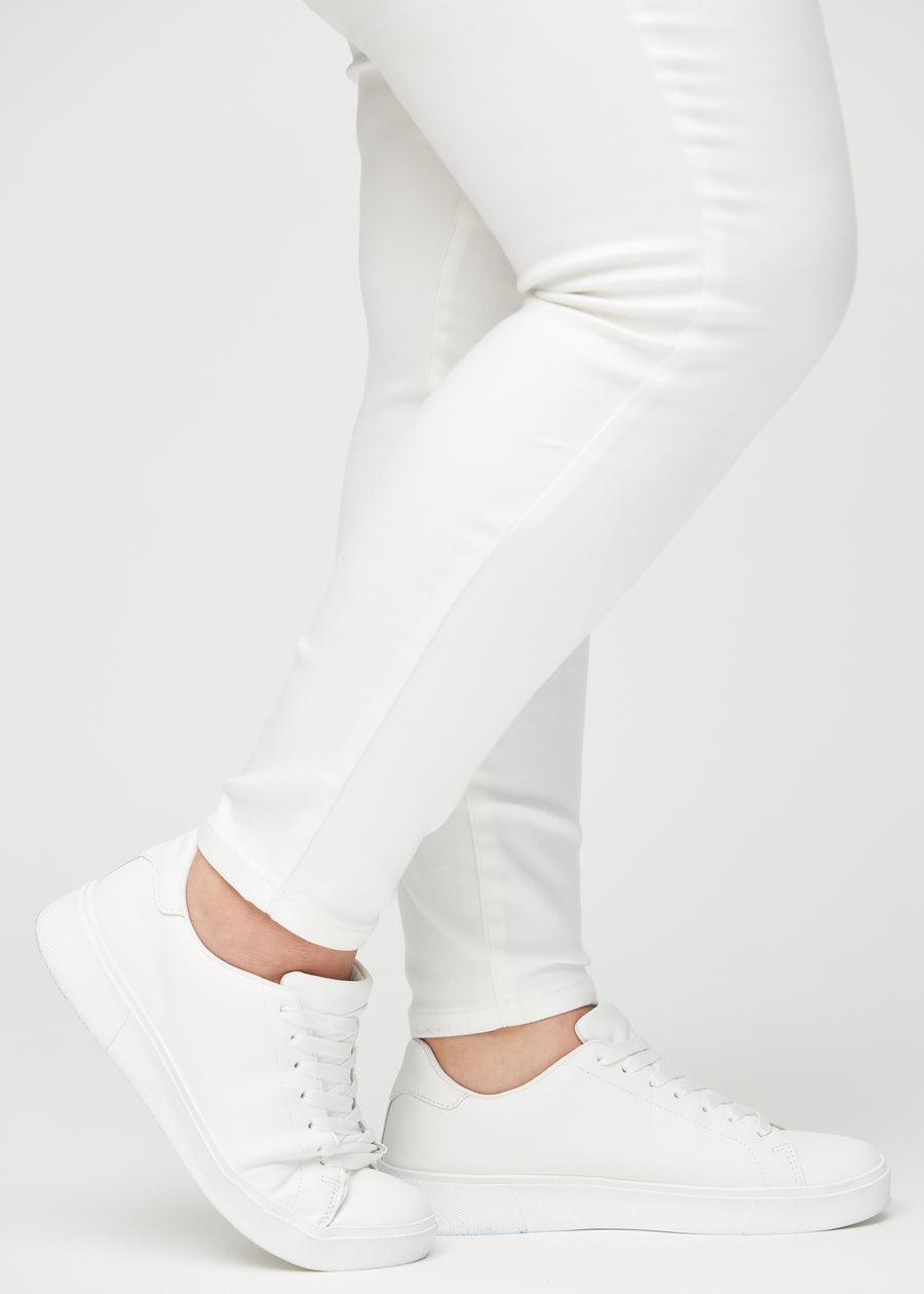 Skinnyjeans för kvinnor i vit, färgen Marguerites. Närbild vid anklarna på en plus size-modell som visar de åtsittande bensluten.