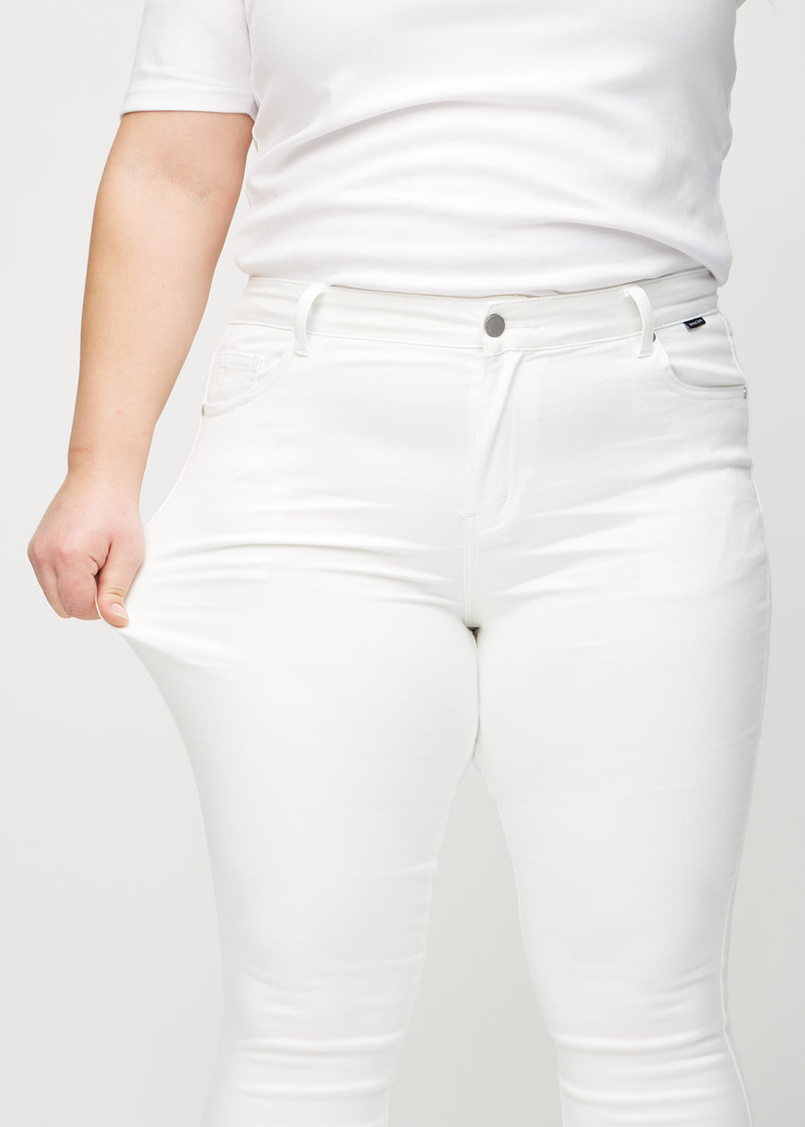 Skinnyjeans för kvinnor i vit, färgen Marguerites. En plus size-modell drar i jeanstyget vid låret för att visa stretchen.