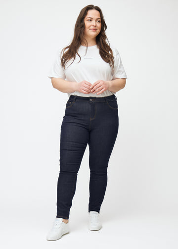 Helbild av plus-size-modell i djup mörkblå denim jeans för kvinnor i färgen Midnights med skinny passform.