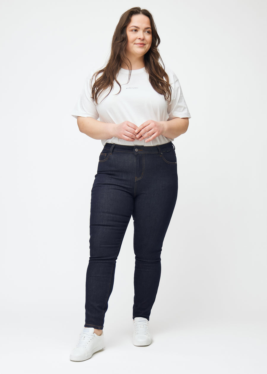 Helbild av plus-size-modell i djup mörkblå denim jeans för kvinnor i färgen Midnights med skinny passform.