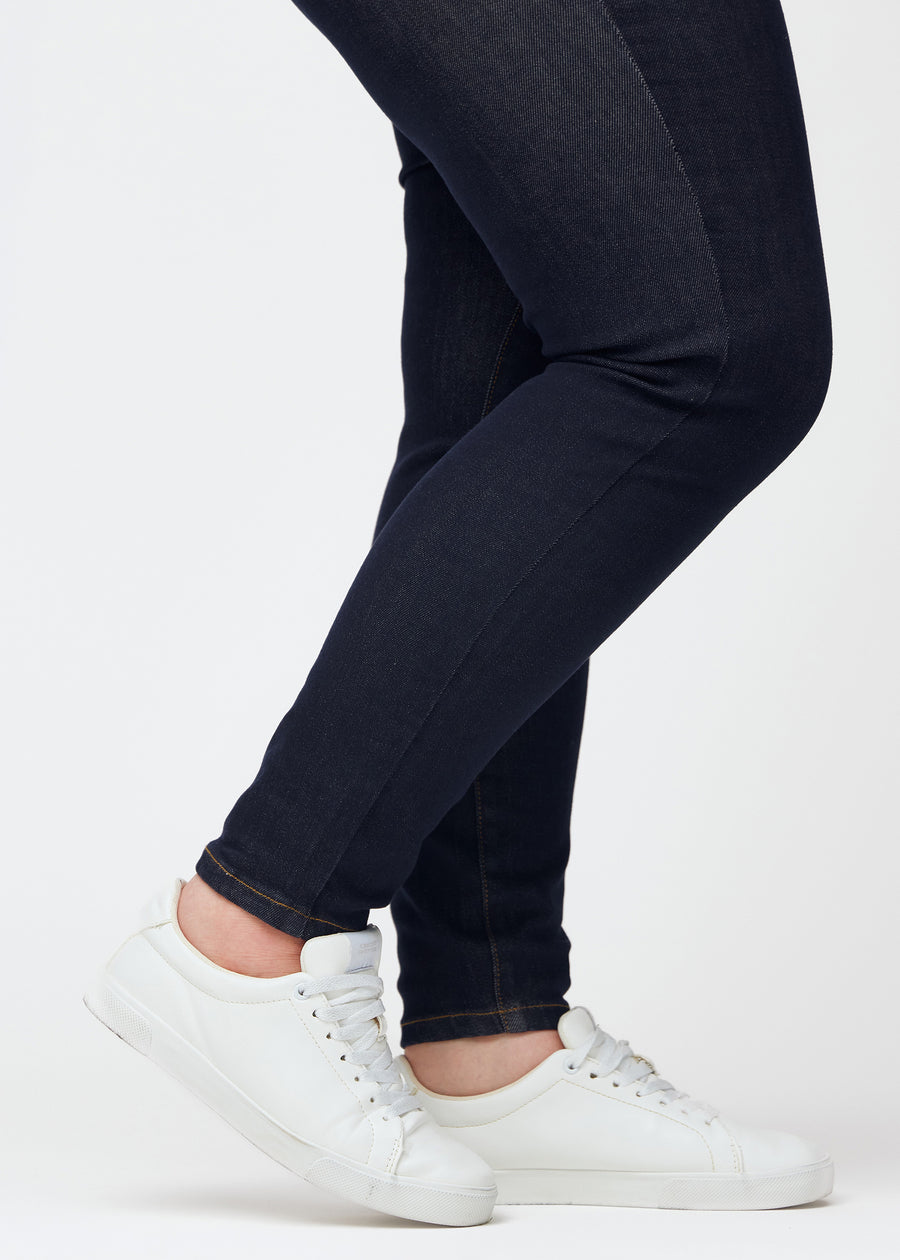 Djup mörkblå denim jeans för kvinnor i färgen Midnights med skinny passform sedd i närbild vid anklarna på plus-size-modell för att visa den tätsittande avslutningen.