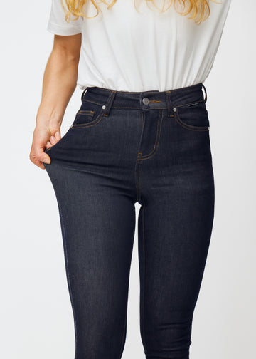Modellen sträcker den djupa mörkblå denimen jeans för kvinnor i färgen Midnights vid låret för att visa materialets stretch.