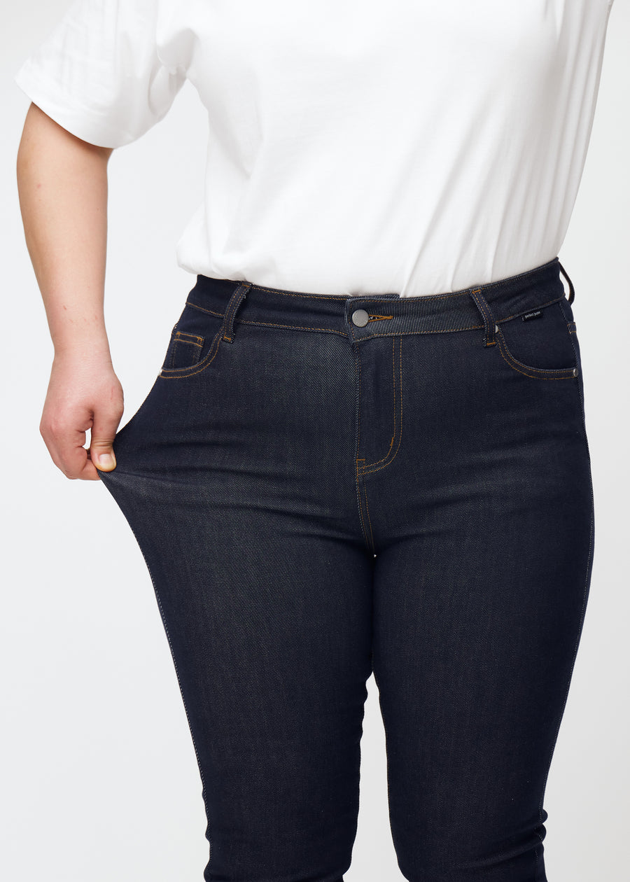 Plus-size-modell sträcker den djupa mörkblå denimen jeans för kvinnor i färgen Midnights vid låret för att visa materialets stretch.