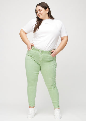 Helbild av en plus-size-modell i ljusgröna skinny jeans.