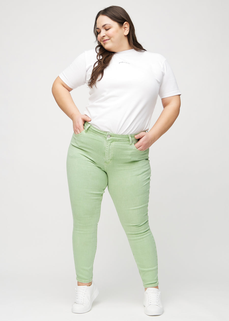 Helbild av en plus-size-modell i ljusgröna skinny jeans.