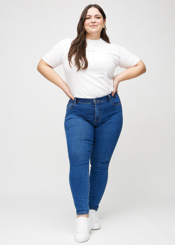 Skinnyjeans för kvinnor i mörkblå, färgen Oceans. Helbild av en plus size-modell i jeansen.