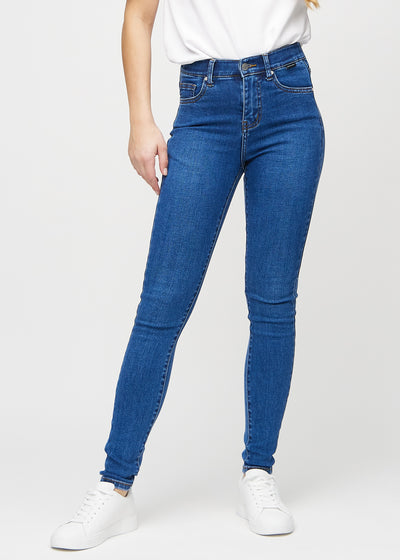 Skinnyjeans för kvinnor i mörkblå, färgen Oceans. Framifrån på en modell, med nära passform runt benen.