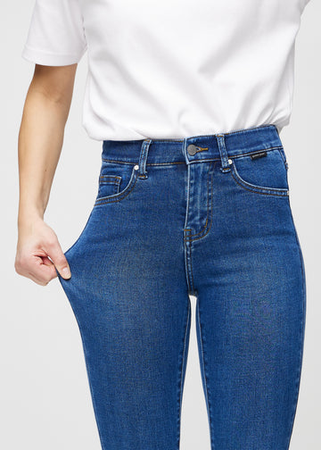 Skinnyjeans för kvinnor i mörkblå, färgen Oceans. En modell drar i jeanstyget vid låret för att visa stretchen.