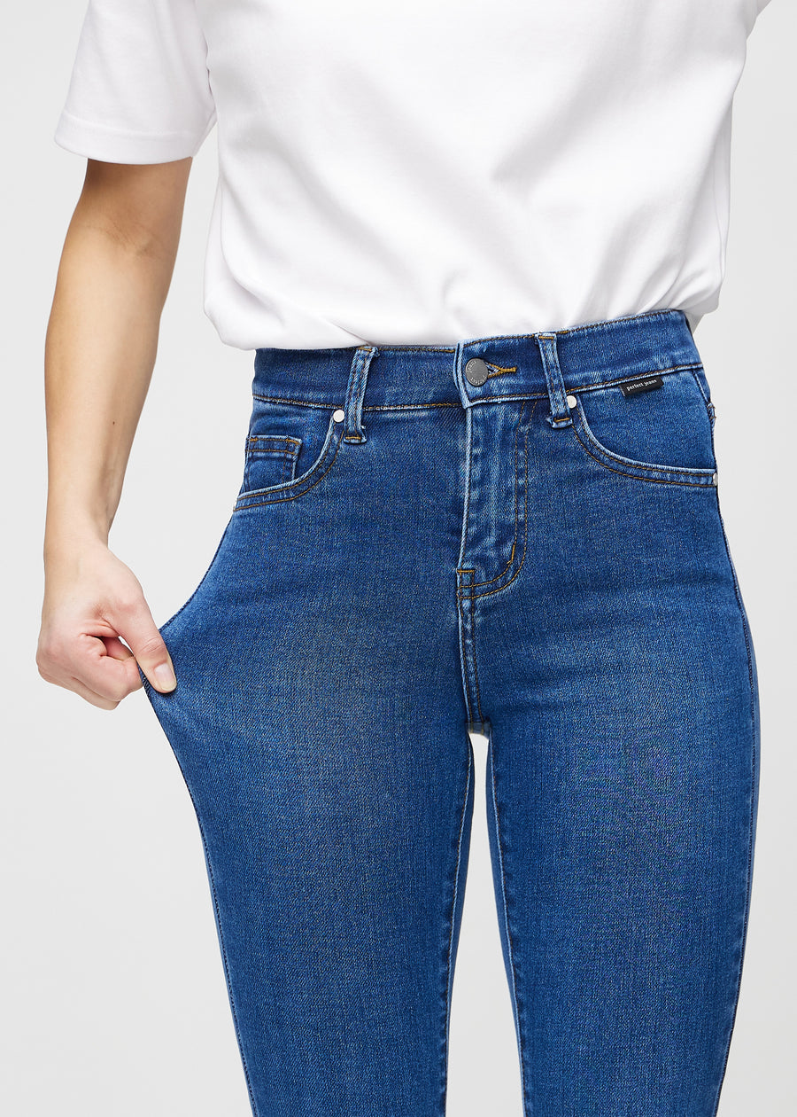 Skinnyjeans för kvinnor i mörkblå, färgen Oceans. En modell drar i jeanstyget vid låret för att visa stretchen.