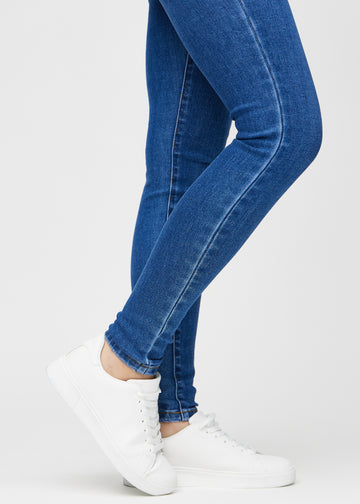 Skinnyjeans för kvinnor i mörkblå, färgen Oceans. Närbild vid anklarna på en modell som visar de åtsittande bensluten.