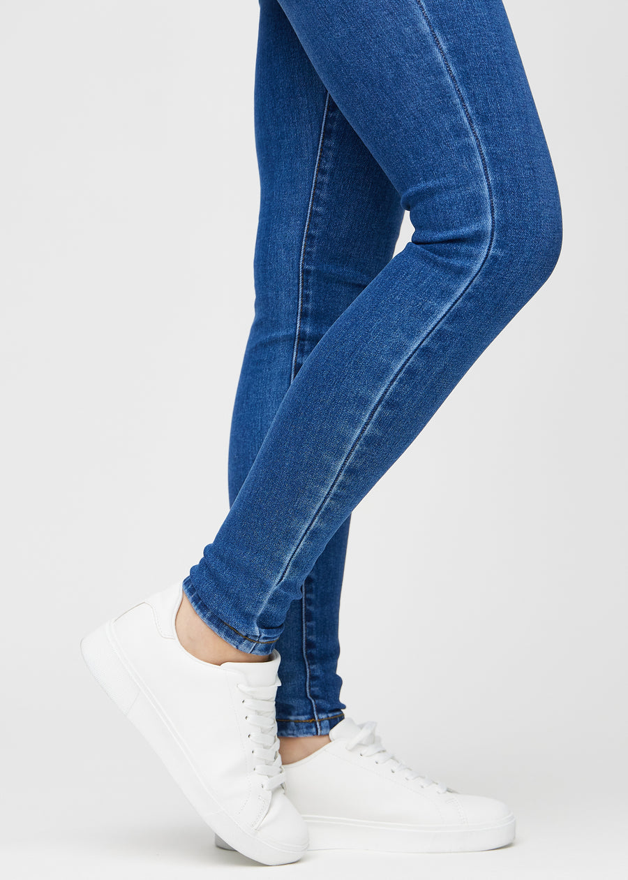 Skinnyjeans för kvinnor i mörkblå, färgen Oceans. Närbild vid anklarna på en modell som visar de åtsittande bensluten.