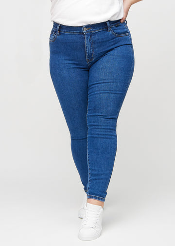 Skinnyjeans för kvinnor i mörkblå, färgen Oceans. Framifrån på en plus size-modell, med nära passform runt benen.