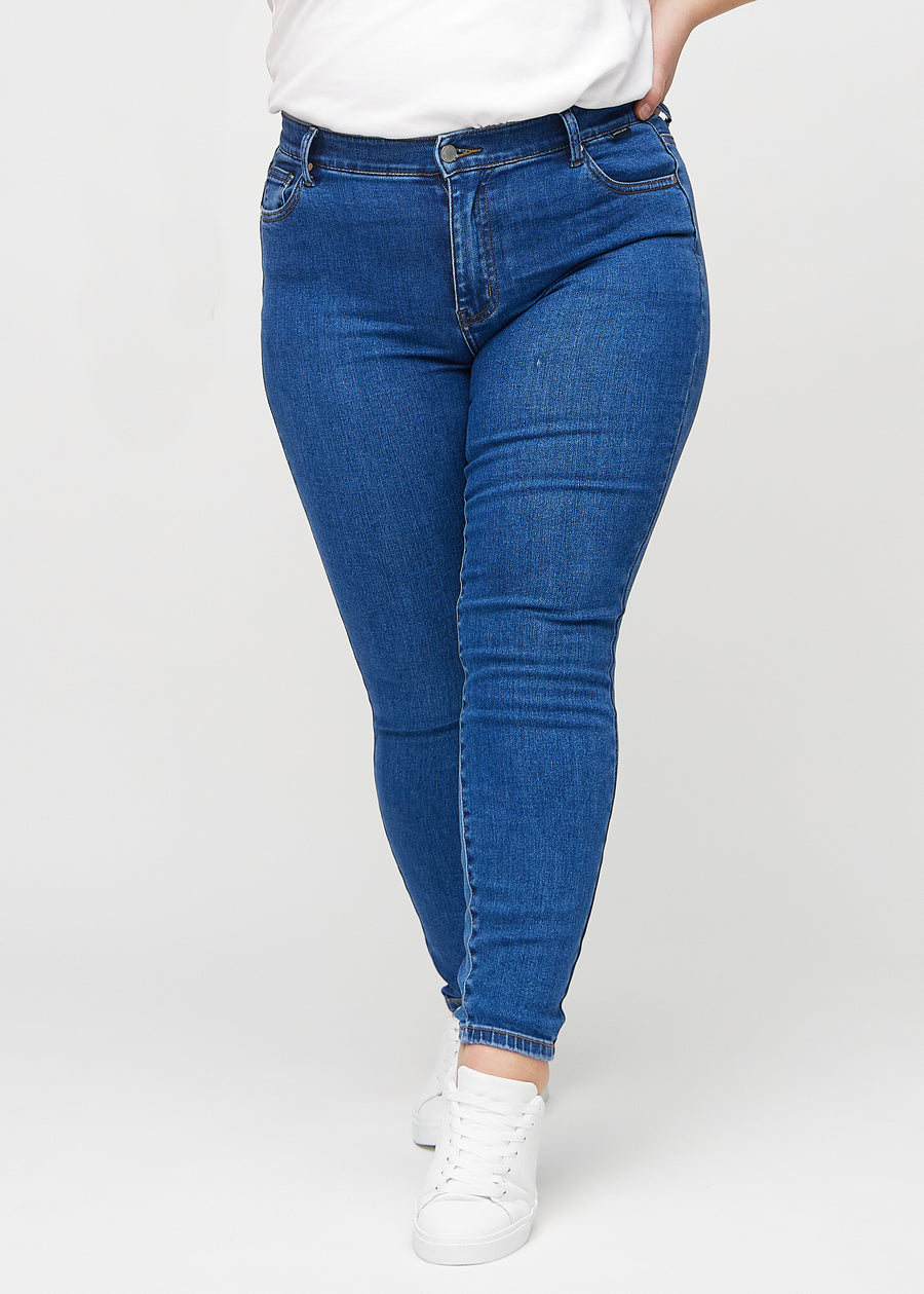 Skinnyjeans för kvinnor i mörkblå, färgen Oceans. Framifrån på en plus size-modell, med nära passform runt benen.