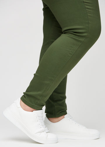 Skinnyjeans för kvinnor i mörkgrön, färgen Renewals. Närbild vid anklarna på en plus size-modell som visar de åtsittande bensluten.