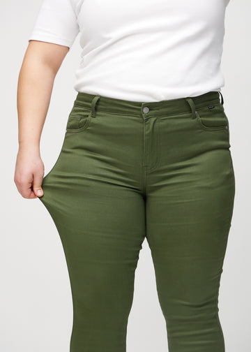 Skinnyjeans för kvinnor i mörkgrön, färgen Renewals. En plus size-modell drar i jeanstyget vid låret för att visa stretchen.