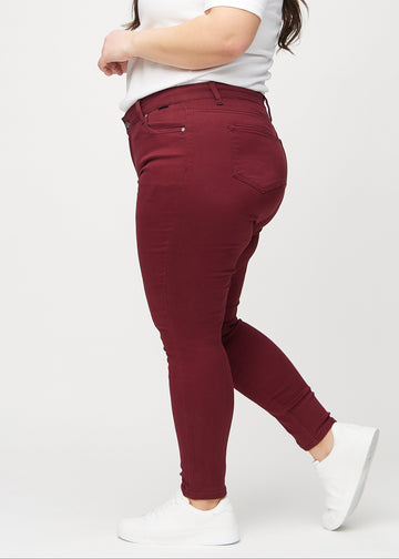 Skinnyjeans för kvinnor i mörkröd, färgen Santas. Från sidan på en plus size-modell.