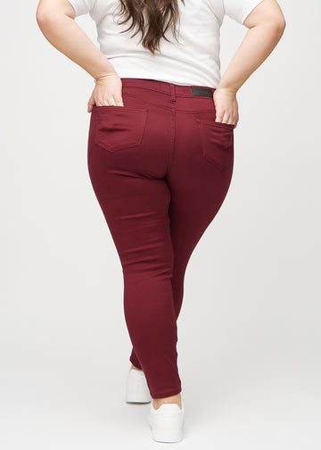 Skinnyjeans för kvinnor i mörkröd, färgen Santas. Bakifrån på en plus size-modell, så att hela passformen syns.