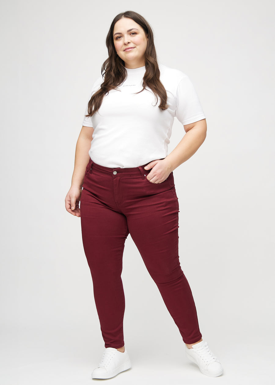 Skinnyjeans för kvinnor i mörkröd, färgen Santas. Helbild av en plus size-modell i jeansen.