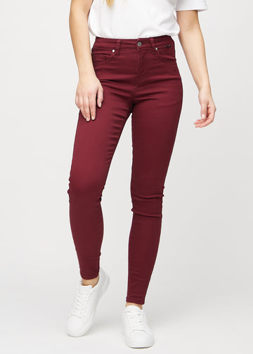 Skinnyjeans för kvinnor i mörkröd, färgen Santas. Framifrån på en modell, med nära passform runt benen.