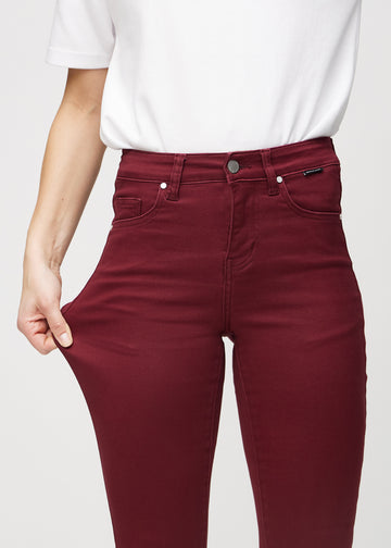 Skinnyjeans för kvinnor i mörkröd, färgen Santas. En modell drar i jeanstyget vid låret för att visa stretchen.
