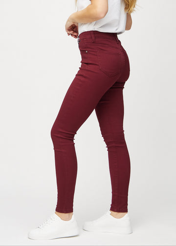 Skinnyjeans för kvinnor i mörkröd, färgen Santas. Från sidan på en modell.