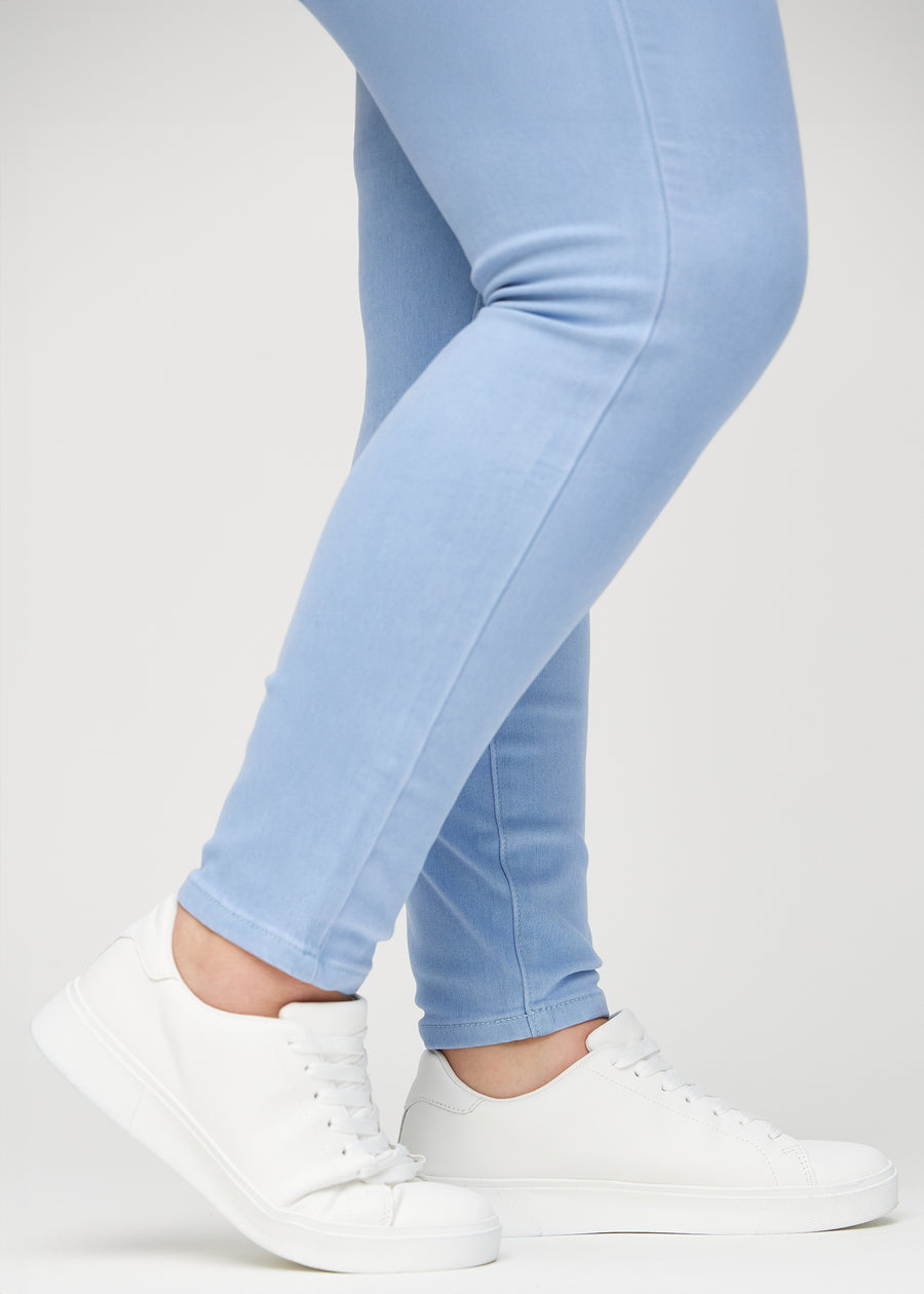 Skinnyjeans för kvinnor i ljusblå, färgen Skies. Närbild vid anklarna på en plus size-modell som visar de åtsittande bensluten.