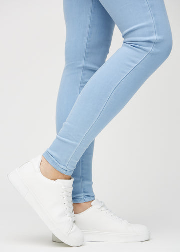 Skinnyjeans för kvinnor i ljusblå, färgen Skies. Närbild vid anklarna på en modell som visar de åtsittande bensluten.