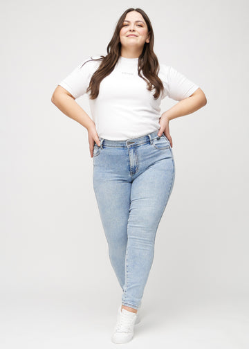 Skinnyjeans för kvinnor i ljusblå, färgen Waves. Helbild av en plus size-modell i jeansen.
