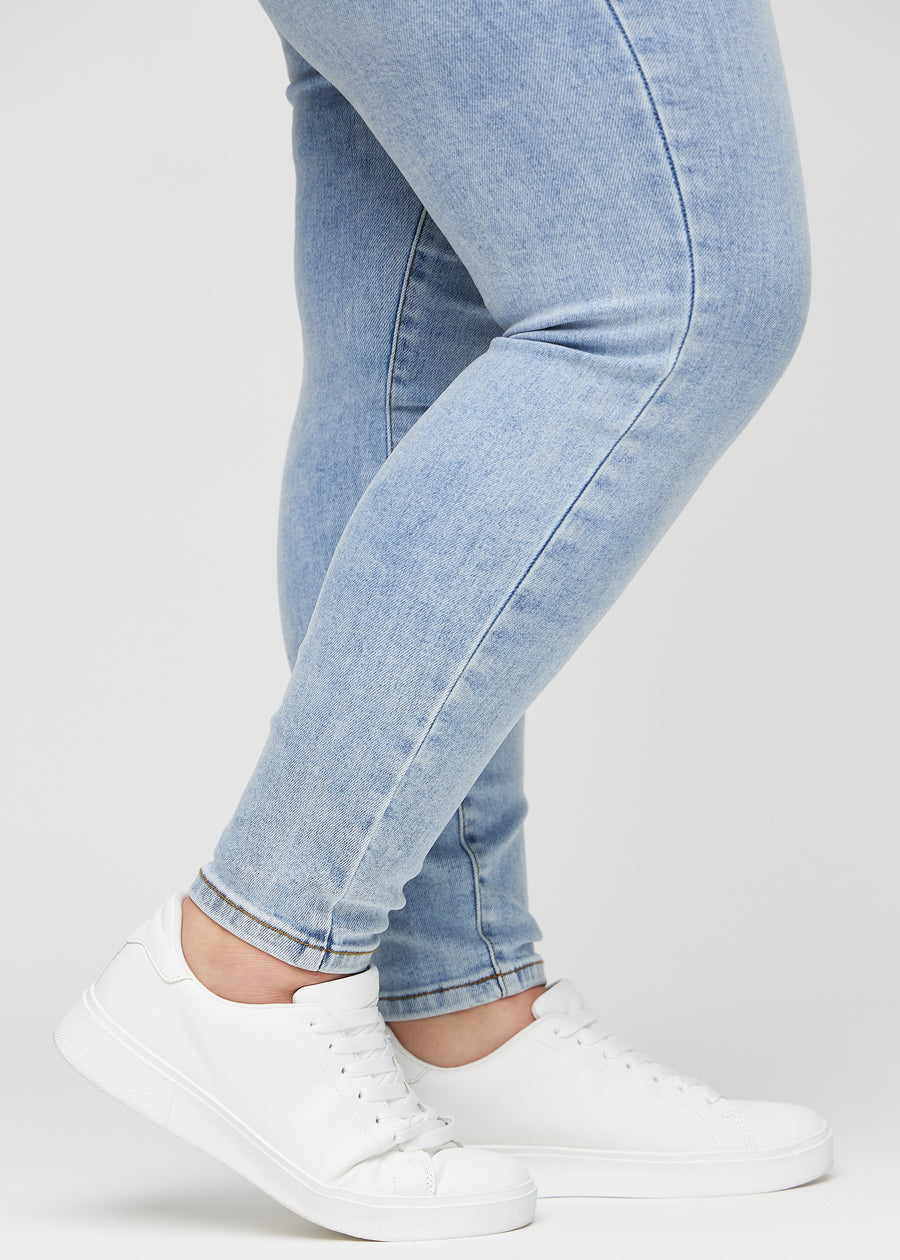 Skinnyjeans för kvinnor i ljusblå, färgen Waves. Närbild vid anklarna på en plus size-modell som visar de åtsittande bensluten.