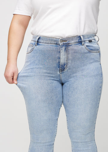 Skinnyjeans för kvinnor i ljusblå, färgen Waves. En plus size-modell drar i jeanstyget vid låret för att visa stretchen.