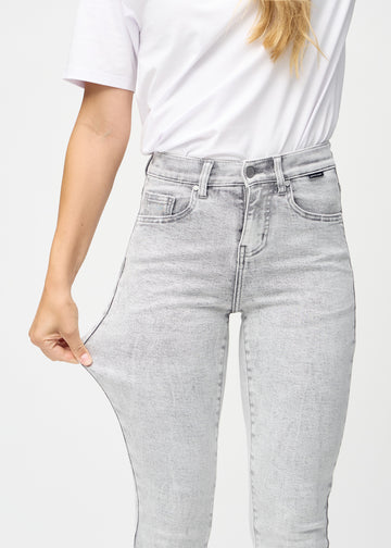 Slimjeans för kvinnor i ljusgrå, färgen Ashes. En modell drar i jeanstyget vid låret för att visa stretchen.